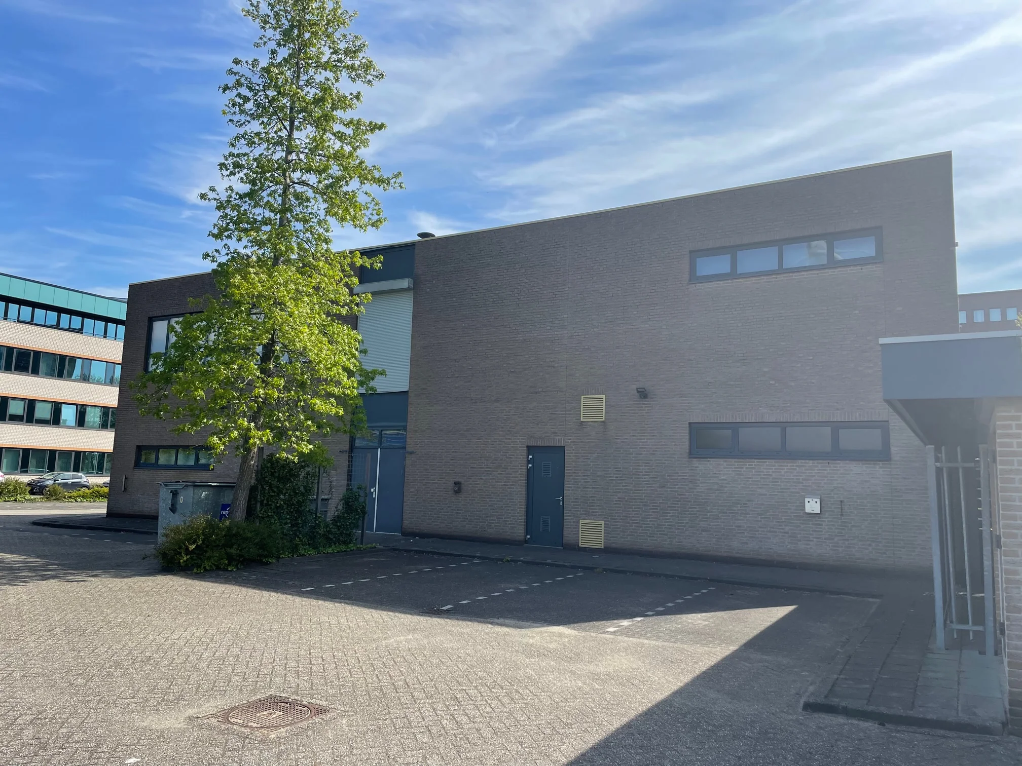 Bedrijfspand aan de Rivium 4e Straat met parkeerplaatsen en een boom op de voorgrond.